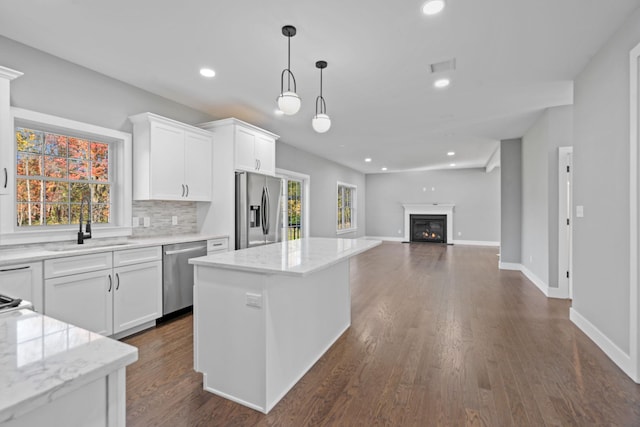 kitchen with a kitchen island, a sink, stainless steel appliances, white cabinetry, and tasteful backsplash