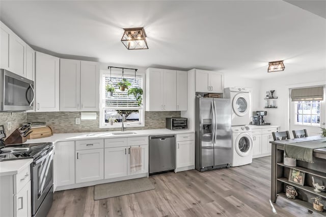 kitchen featuring sink, light hardwood / wood-style flooring, stainless steel appliances, stacked washing maching and dryer, and white cabinets