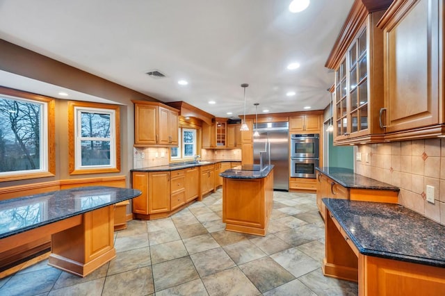 kitchen featuring a kitchen island, appliances with stainless steel finishes, tasteful backsplash, dark stone countertops, and hanging light fixtures