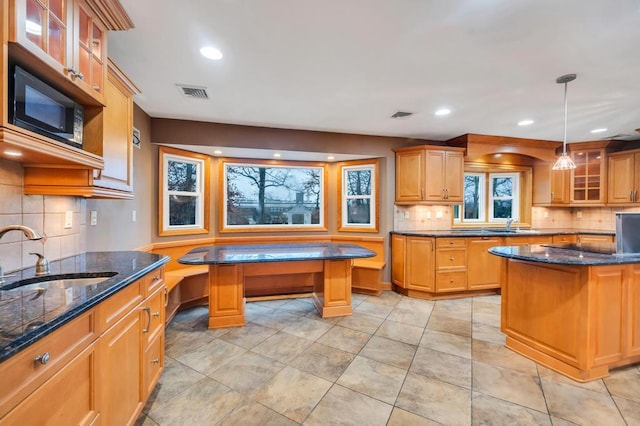 kitchen with a kitchen island, sink, dark stone countertops, and decorative light fixtures