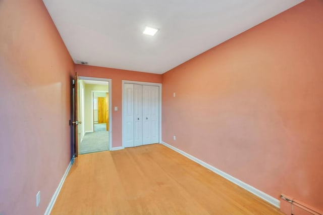 unfurnished bedroom featuring light hardwood / wood-style flooring, a baseboard radiator, and a closet