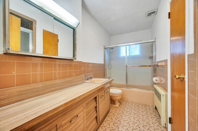 full bathroom featuring toilet, combined bath / shower with glass door, tile walls, vanity, and radiator