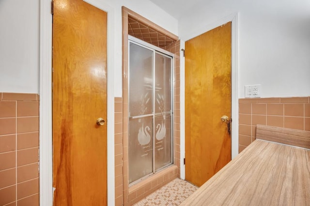 bathroom with a shower with door and tile walls