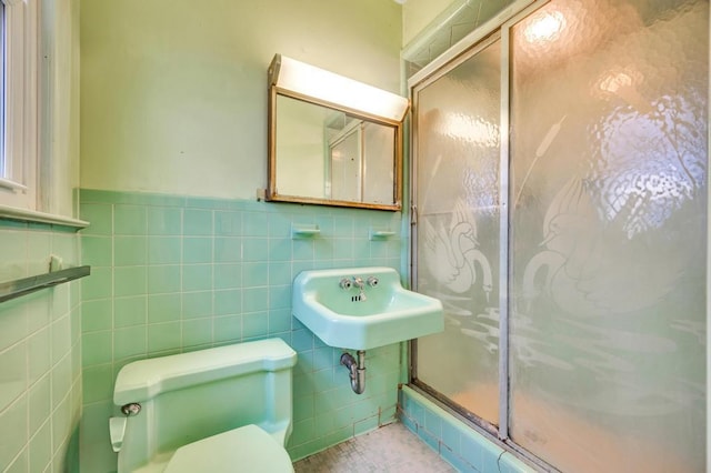 bathroom featuring tile walls, sink, a shower with door, and toilet