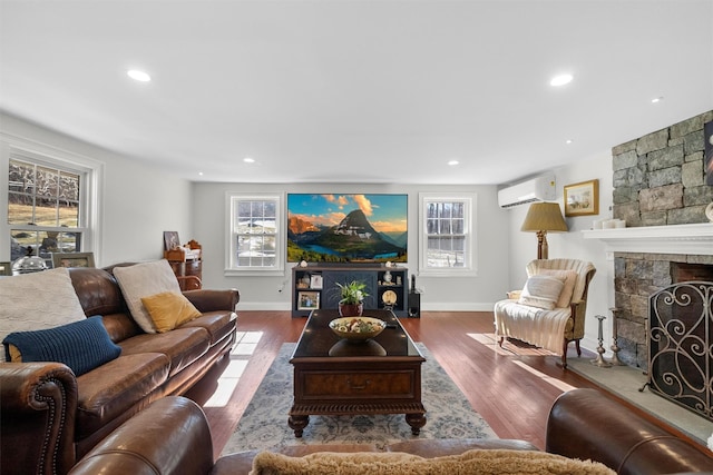 living room with wood-type flooring, an AC wall unit, and a fireplace