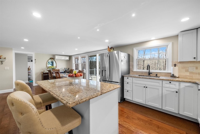 kitchen featuring sink, white cabinetry, stainless steel fridge, a wall unit AC, and a kitchen island