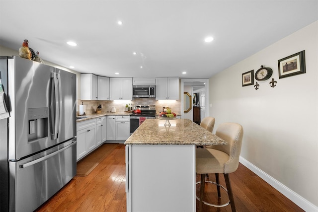 kitchen featuring a breakfast bar area, white cabinetry, stainless steel appliances, light stone countertops, and a kitchen island