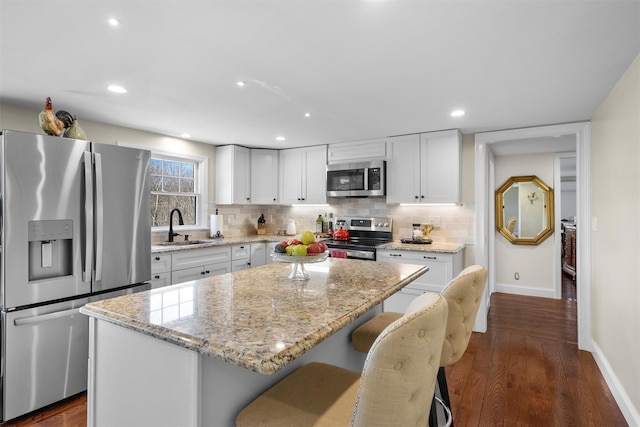 kitchen with sink, appliances with stainless steel finishes, white cabinetry, light stone countertops, and a kitchen island