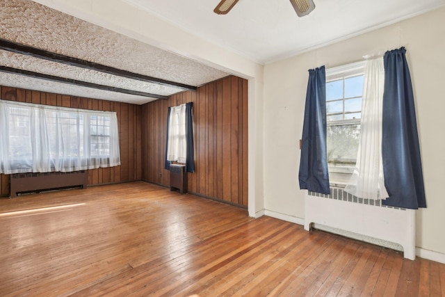 empty room featuring beam ceiling, radiator, and light hardwood / wood-style floors