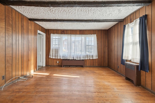 empty room featuring wood walls, a textured ceiling, light wood-type flooring, radiator heating unit, and beamed ceiling