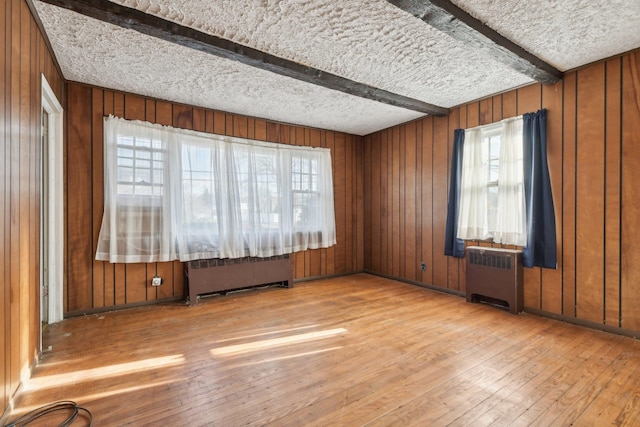 spare room with light hardwood / wood-style flooring, a textured ceiling, radiator heating unit, and beamed ceiling