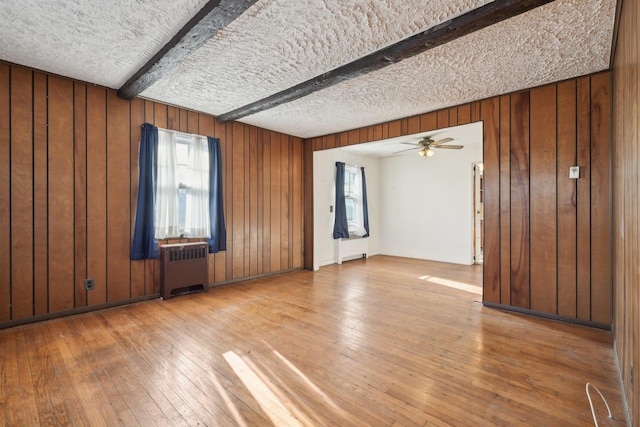 spare room featuring radiator, hardwood / wood-style flooring, a textured ceiling, beamed ceiling, and wood walls