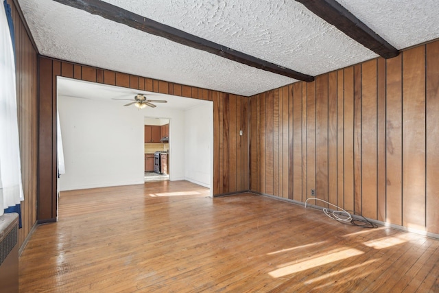 spare room featuring wood-type flooring, wooden walls, a textured ceiling, and beam ceiling