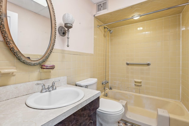 full bathroom with tiled shower / bath, vanity, toilet, and tile walls