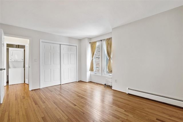 unfurnished bedroom with stacked washer and dryer, a closet, baseboard heating, and light hardwood / wood-style floors