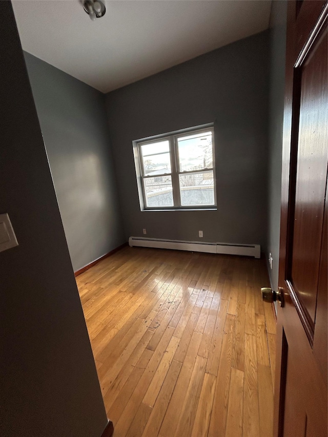 unfurnished room with baseboard heating and light hardwood / wood-style flooring