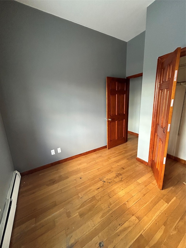 unfurnished bedroom featuring a baseboard heating unit and light wood-type flooring