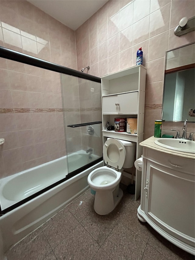 full bathroom with vanity, toilet, combined bath / shower with glass door, and tile walls