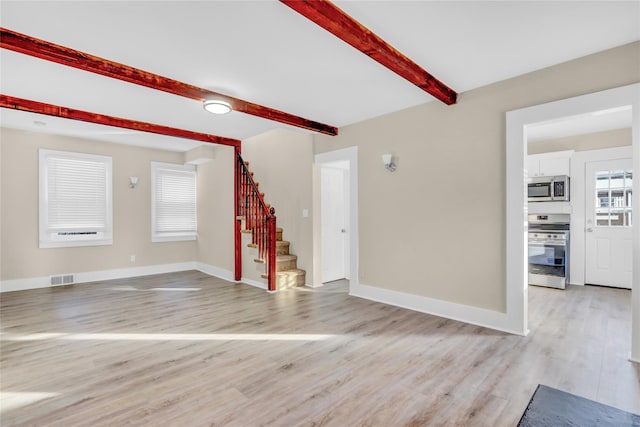 unfurnished living room featuring beamed ceiling and light wood-type flooring