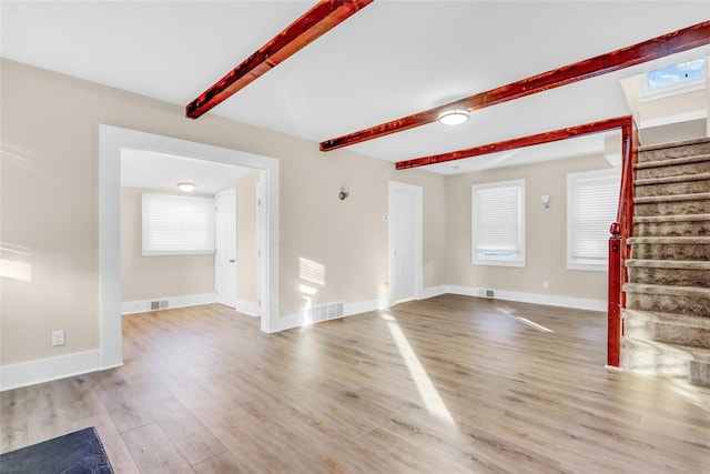 unfurnished living room featuring beamed ceiling and light hardwood / wood-style floors