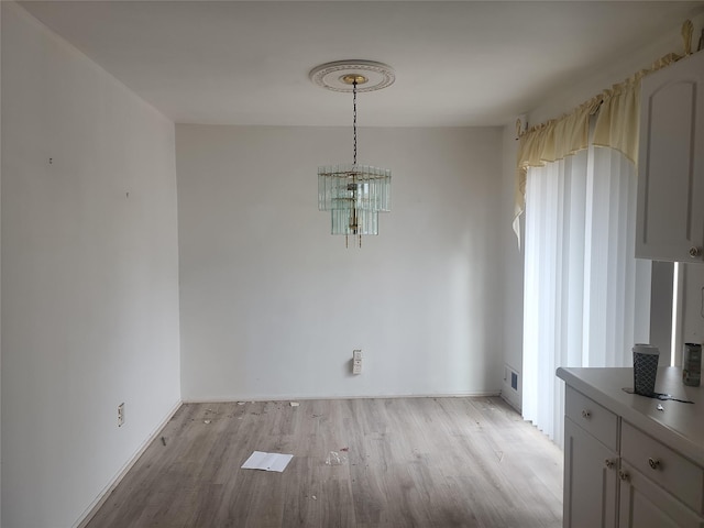 unfurnished dining area with a chandelier and light wood-type flooring