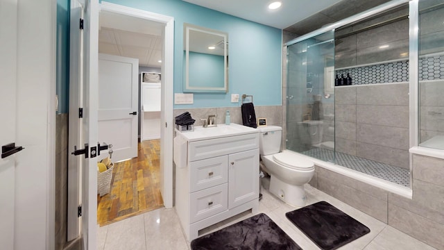 bathroom with tile walls, vanity, a shower with shower door, tile patterned floors, and toilet