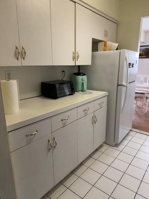 kitchen featuring white refrigerator, light tile patterned floors, and white cabinets