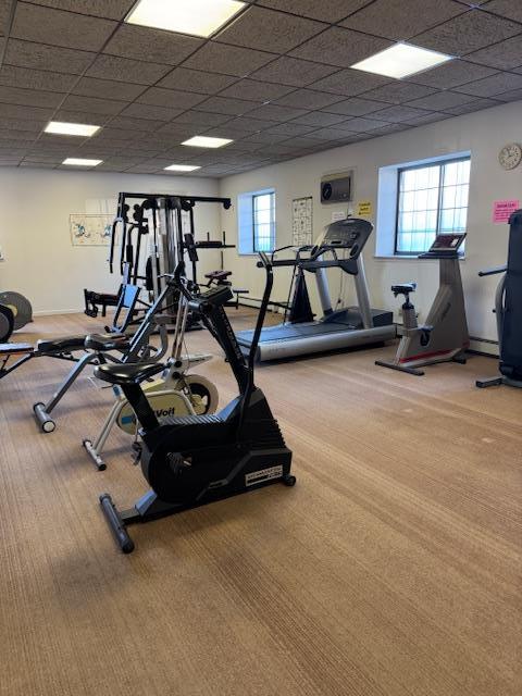 workout area featuring a baseboard heating unit, a paneled ceiling, and light colored carpet