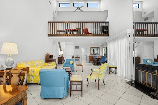 living room featuring stairway, a towering ceiling, a ceiling fan, a glass covered fireplace, and tile patterned floors