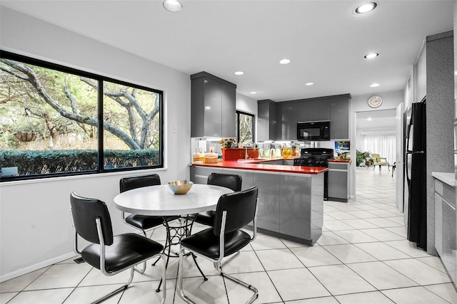 kitchen featuring a peninsula, black appliances, light tile patterned floors, and a wealth of natural light