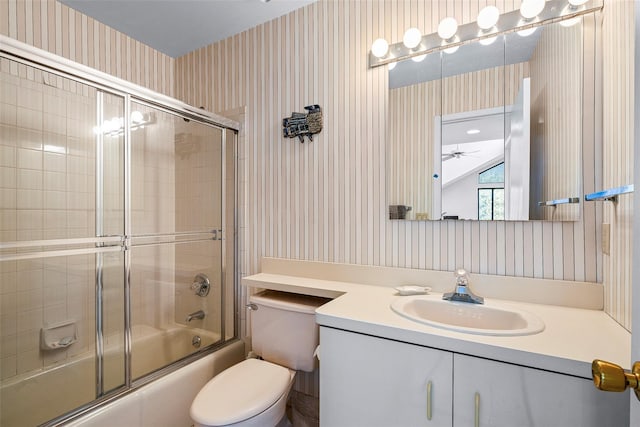 bathroom featuring ceiling fan, toilet, vanity, combined bath / shower with glass door, and wallpapered walls