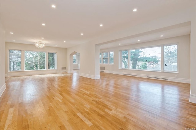 unfurnished living room featuring a notable chandelier, a healthy amount of sunlight, and light wood-type flooring