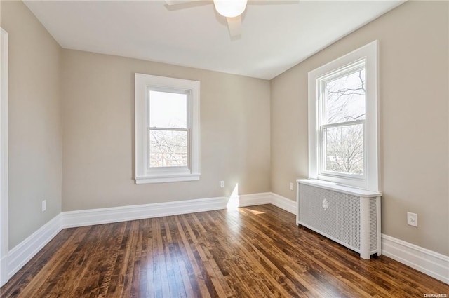 unfurnished room featuring ceiling fan, a wealth of natural light, radiator heating unit, and dark wood-type flooring