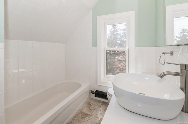 bathroom with a washtub, sink, lofted ceiling, tile walls, and toilet