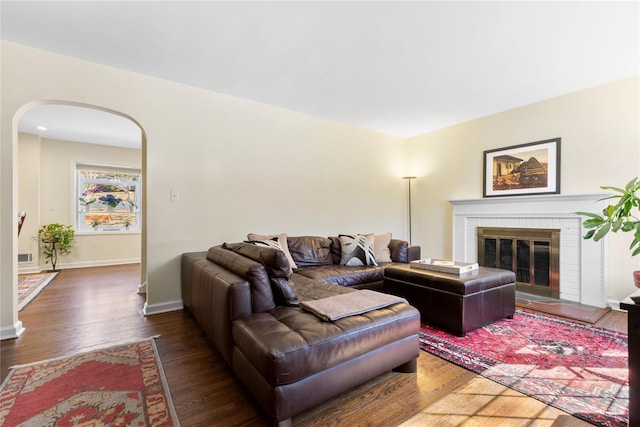 living room featuring a brick fireplace, wood finished floors, arched walkways, and baseboards