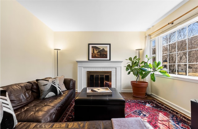 living room with baseboards, a brick fireplace, and wood finished floors