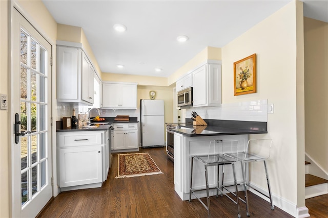 kitchen featuring dark countertops, decorative backsplash, stainless steel appliances, white cabinetry, and a sink