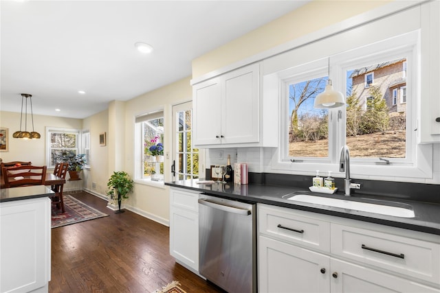 kitchen featuring dark countertops, dark wood-style flooring, stainless steel dishwasher, white cabinetry, and a sink