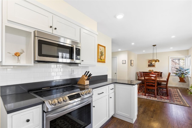 kitchen featuring dark countertops, dark wood-style floors, a peninsula, and stainless steel appliances