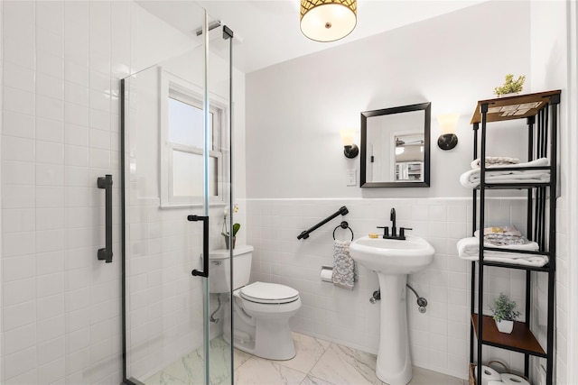 bathroom featuring wainscoting, marble finish floor, tile walls, and a shower stall