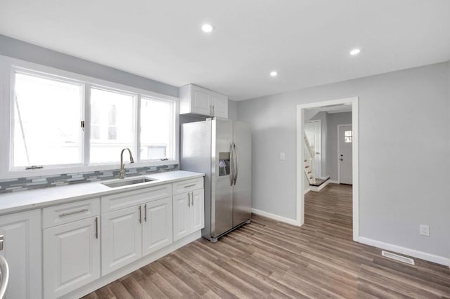 kitchen with stainless steel refrigerator with ice dispenser, sink, light hardwood / wood-style flooring, decorative backsplash, and white cabinets