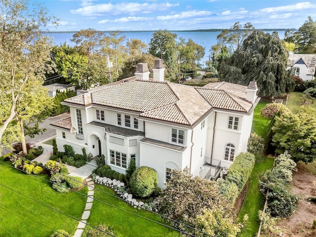 exterior space featuring a tile roof, a chimney, a water view, a front yard, and stucco siding