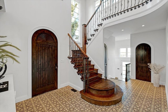 foyer entrance featuring arched walkways, a high ceiling, visible vents, and baseboards