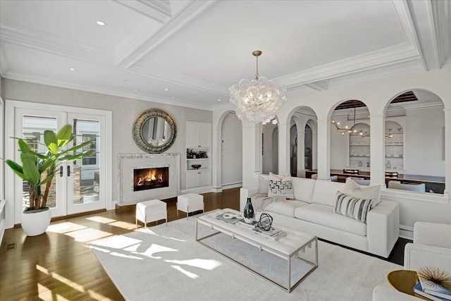 living area featuring arched walkways, wood finished floors, beamed ceiling, an inviting chandelier, and a lit fireplace