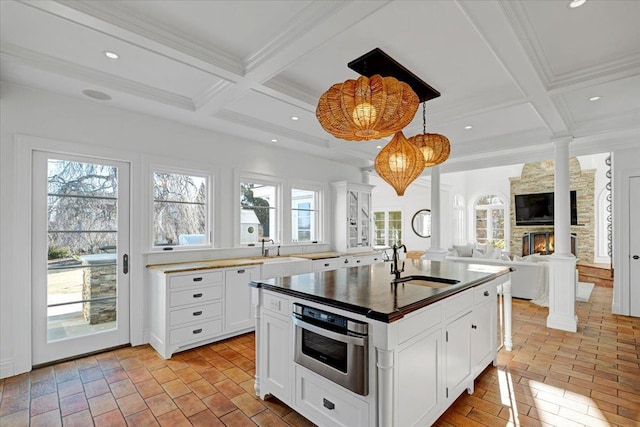 kitchen featuring a fireplace, a center island with sink, decorative columns, stainless steel oven, and a sink