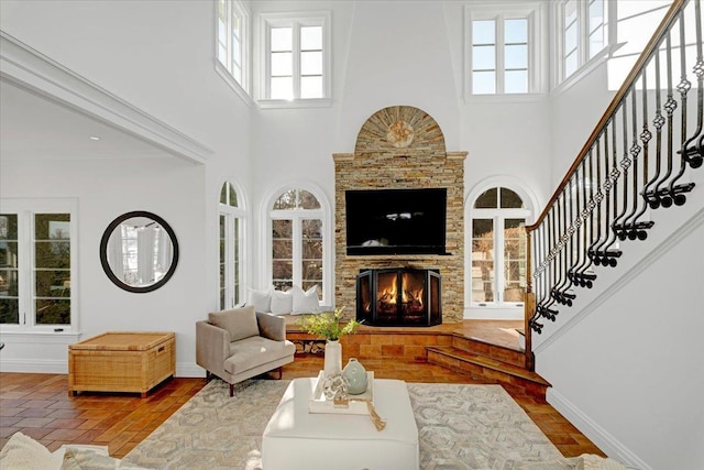 living room featuring a high ceiling, stairs, baseboards, and a stone fireplace