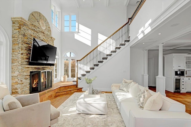 living room featuring a fireplace, wood finished floors, stairs, ornate columns, and crown molding