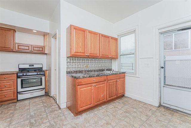 kitchen featuring sink, stainless steel gas range, backsplash, and dark stone counters