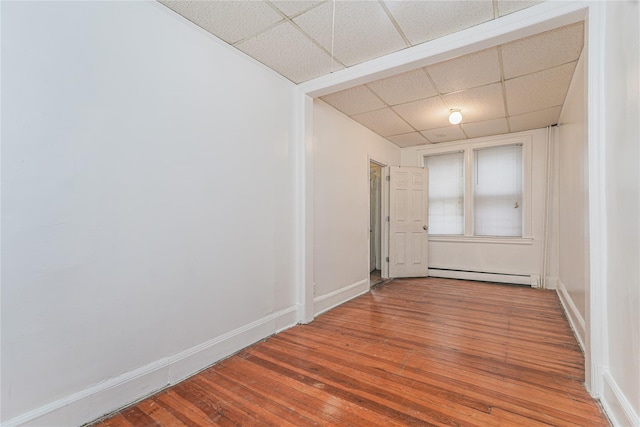 spare room featuring a drop ceiling, a baseboard heating unit, and hardwood / wood-style floors