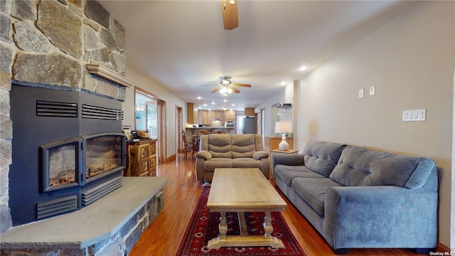 living room featuring ceiling fan, wood-type flooring, and a stone fireplace